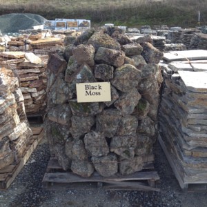 Photo of Black Moss Rock. A flat porous lava rock with black lichen and moss with block like shape. Use for Drystack stone wall, and Masonry Stone Wall. Natural stone sold by Rolleri Landscape Products.